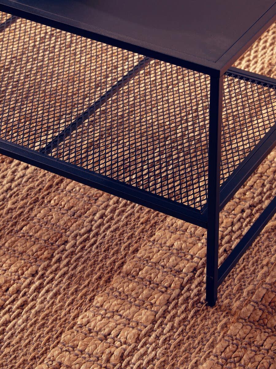 Black metal coffee table with wire mesh shelf on woven jute rug