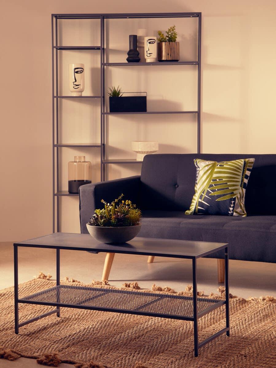 Black metal coffee table with mesh shelf on woven rug, sofa and shelving in background