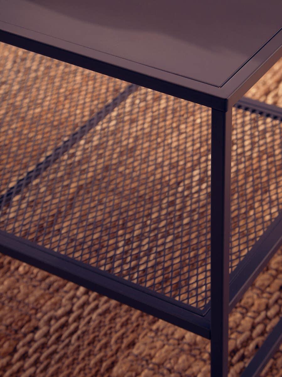 Black metal coffee table with mesh lower shelf on woven rug, close-up view