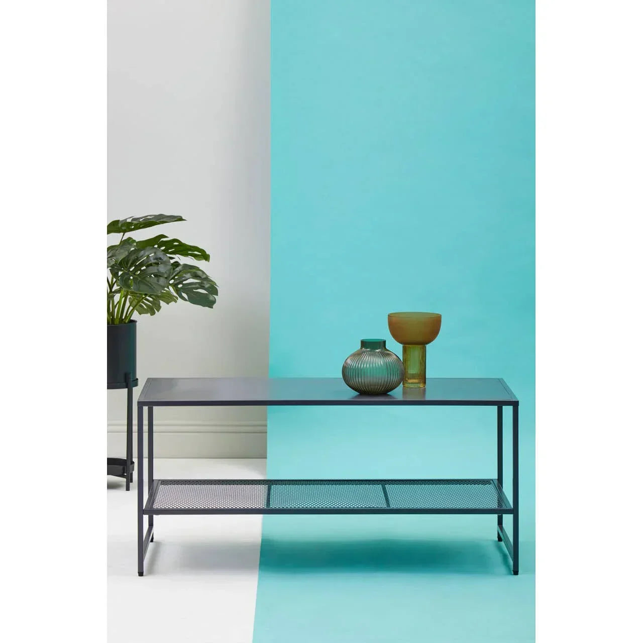 Black metal coffee table with mesh lower shelf, decorative vases, and potted plant beside