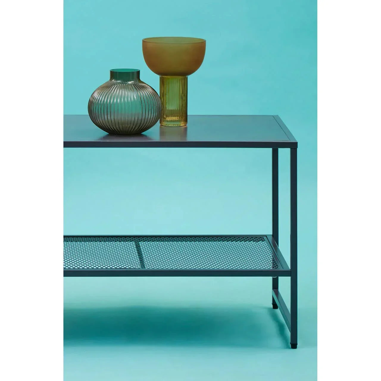 Modern metal coffee table with glass vases and mesh lower shelf on blue background