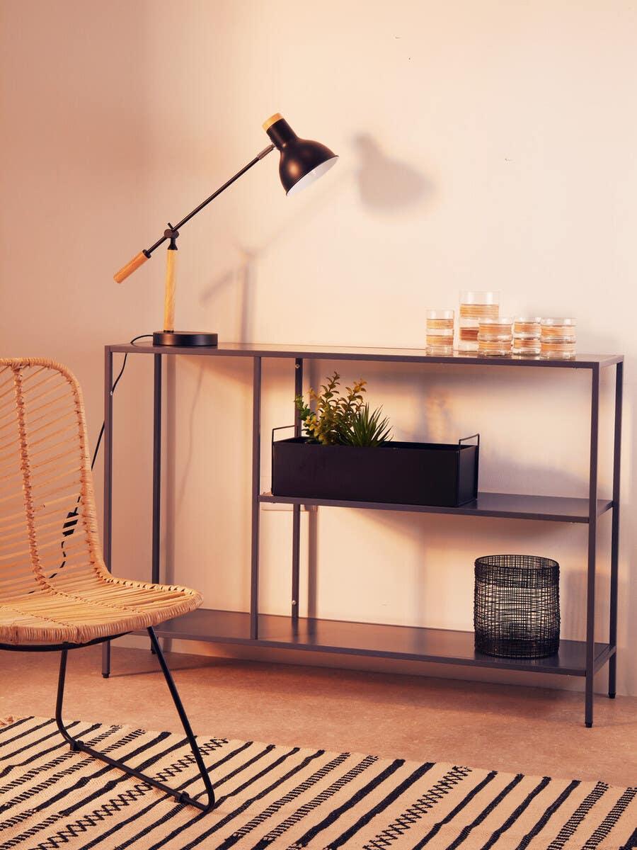 Modern console table with black desk lamp, glass candles, and woven accent chair