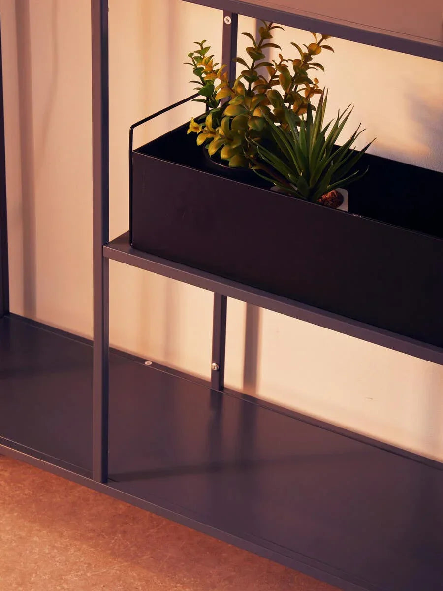 Metal shelving unit with a black planter box holding artificial green plants