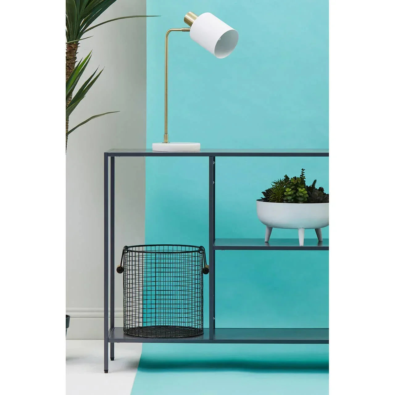 Modern console table with white table lamp, wire basket, and plant on blue background