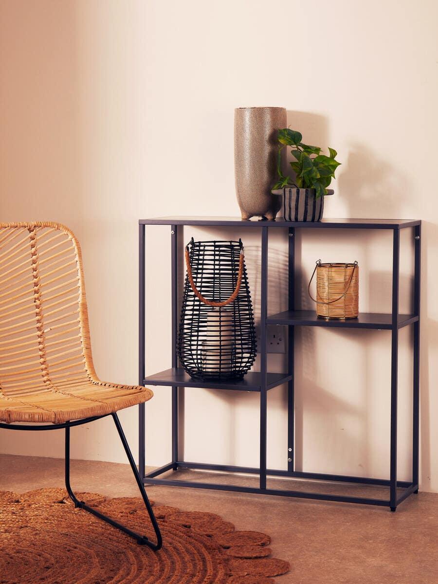 Black metal console table with decorative vases, lanterns, and indoor plant beside rattan chair