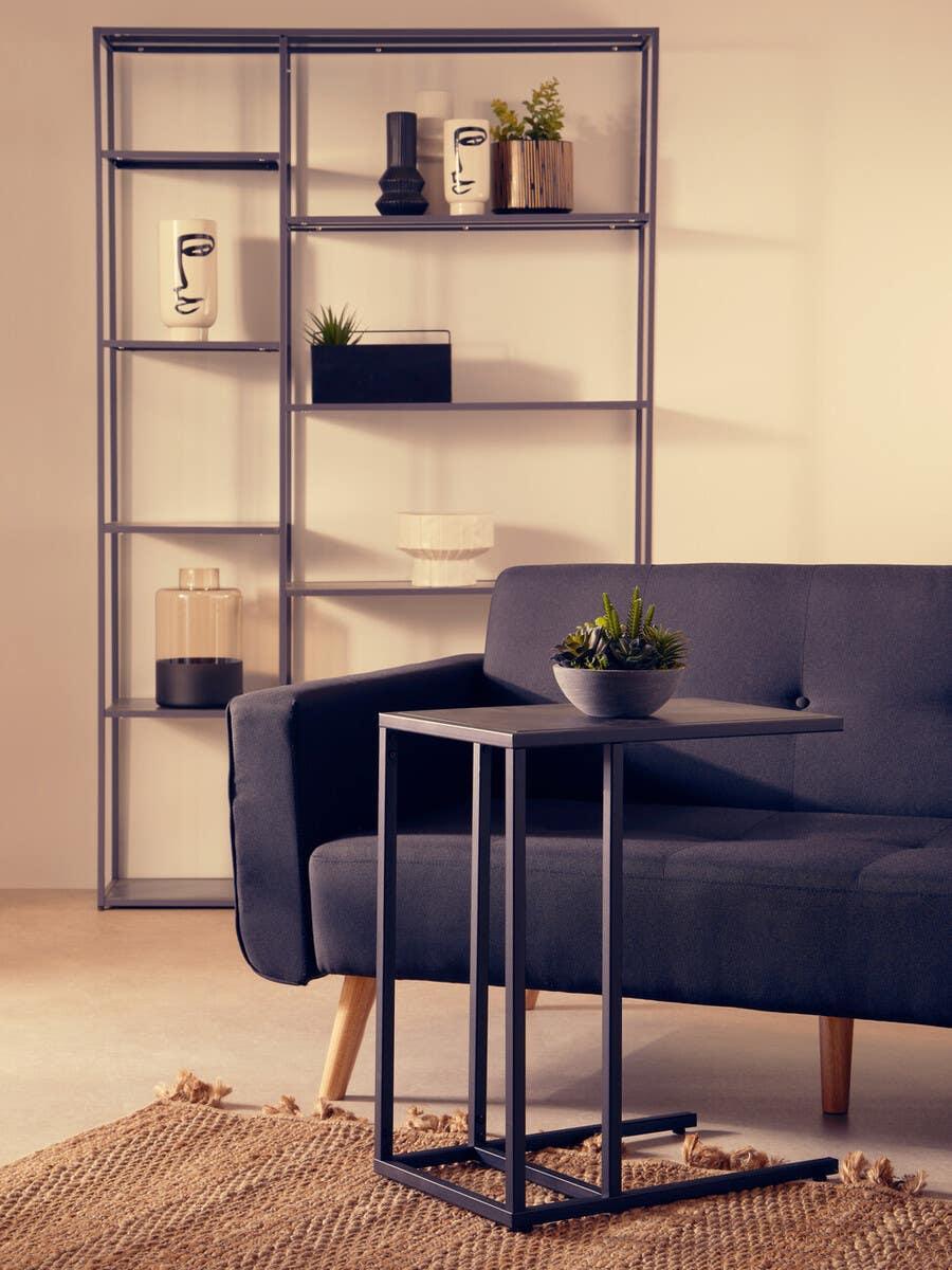 Black metal side table beside dark fabric sofa on jute rug with modern shelving unit