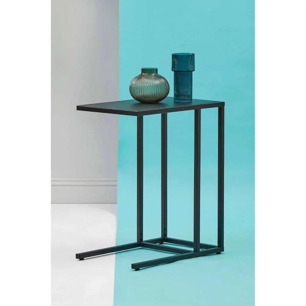 Black metal side table with modern vases on blue background, narrow rectangular design