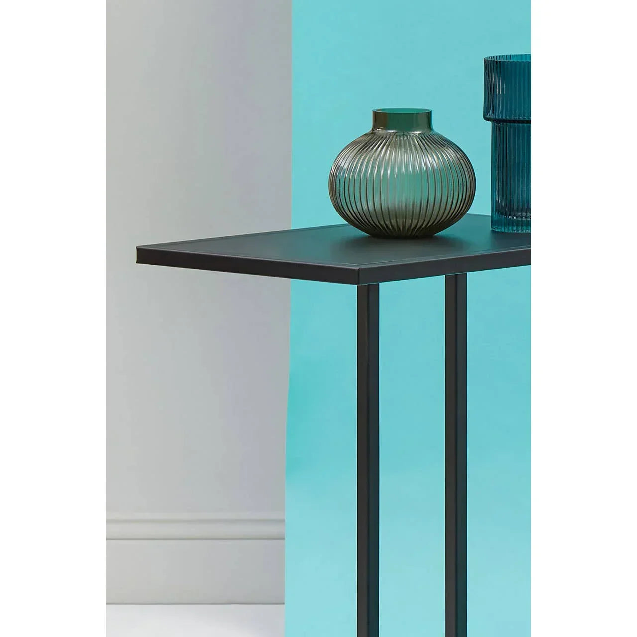 Black metal side table with ribbed glass vase against blue background