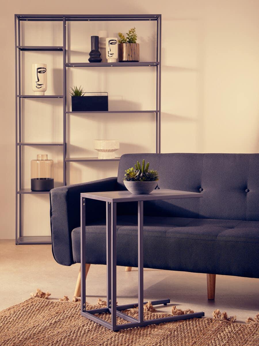Modern grey metal side table with plant beside navy sofa and shelving unit in living room