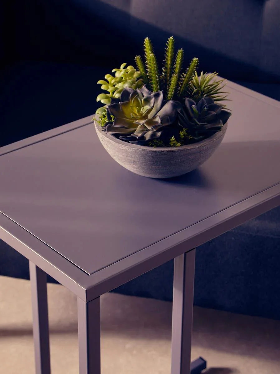 Grey metal side table with artificial succulent plant bowl beside sofa