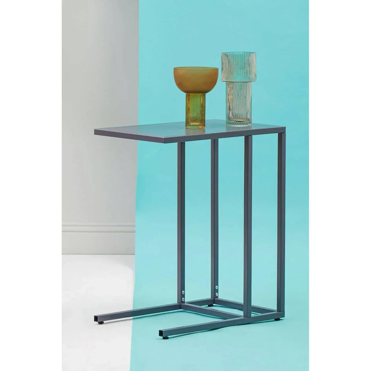 Slim metal side table with two decorative glass vases against a blue background