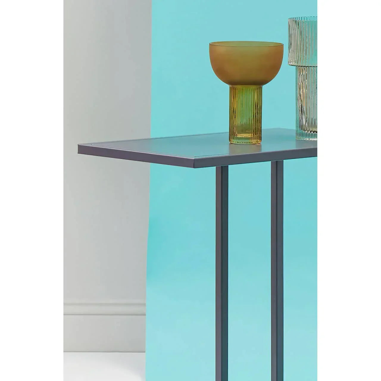 Modern glass side table with slim black legs and amber glass vase on top