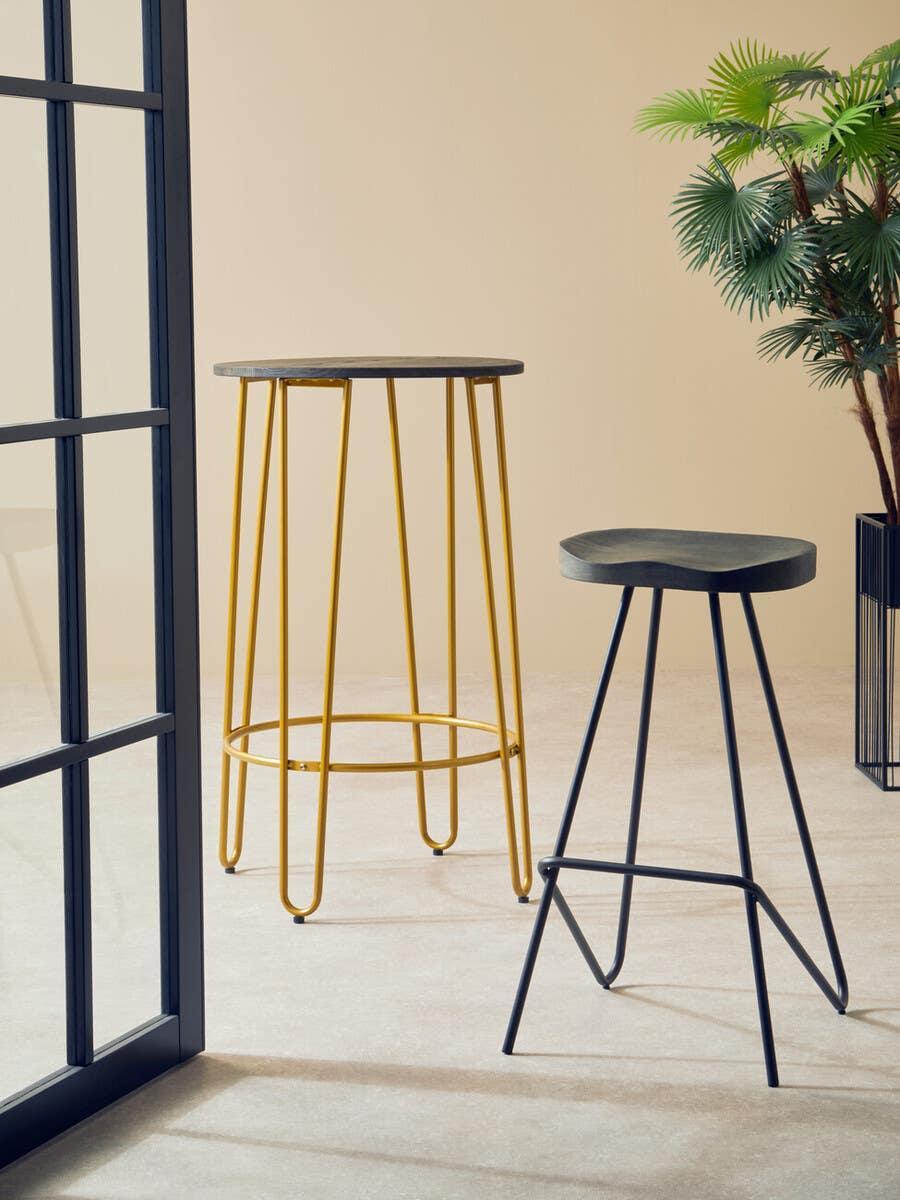 Modern bar table with yellow metal legs and black stool in minimalist room with plant