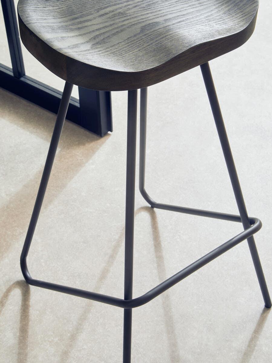 Modern wooden bar stool with contoured seat and black metal legs on tiled floor