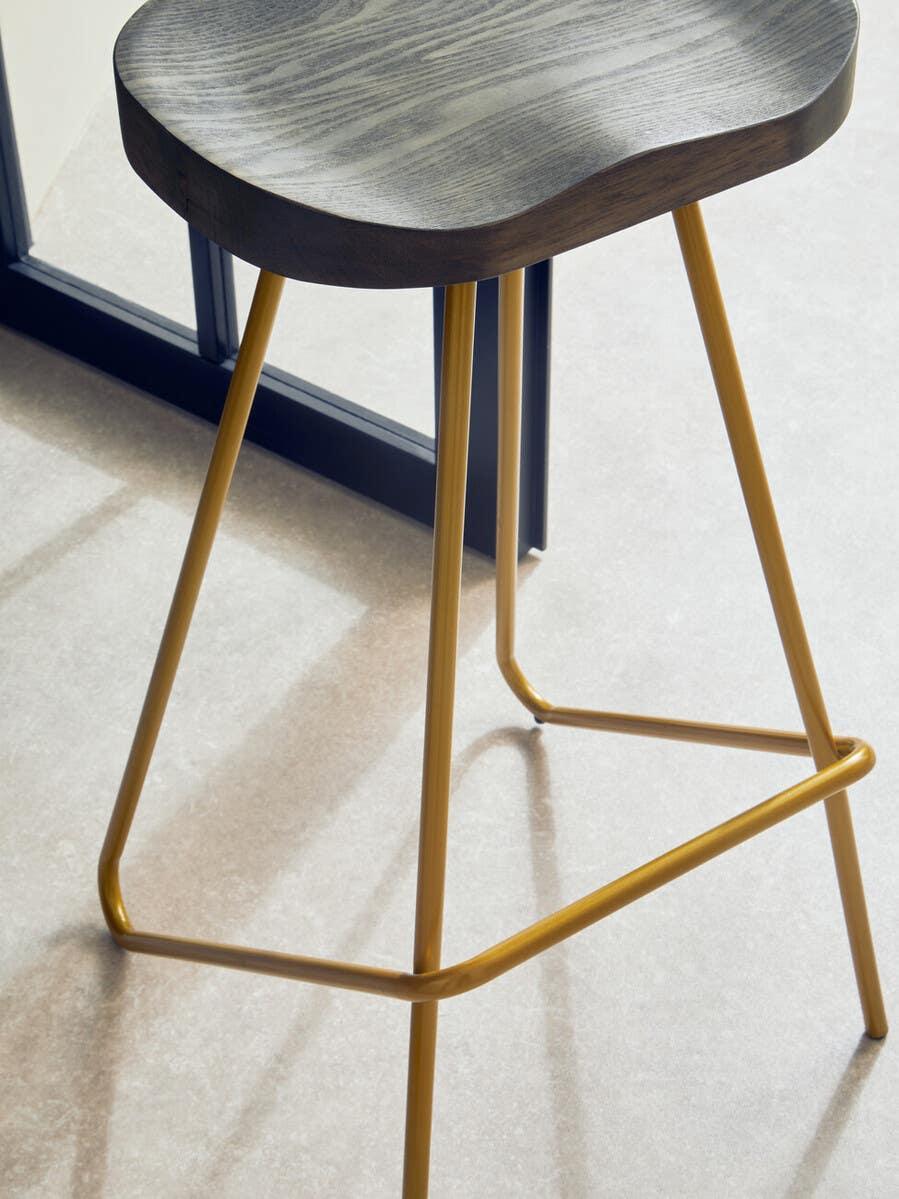 Bar stool with dark wood seat and gold metal legs on light tile floor