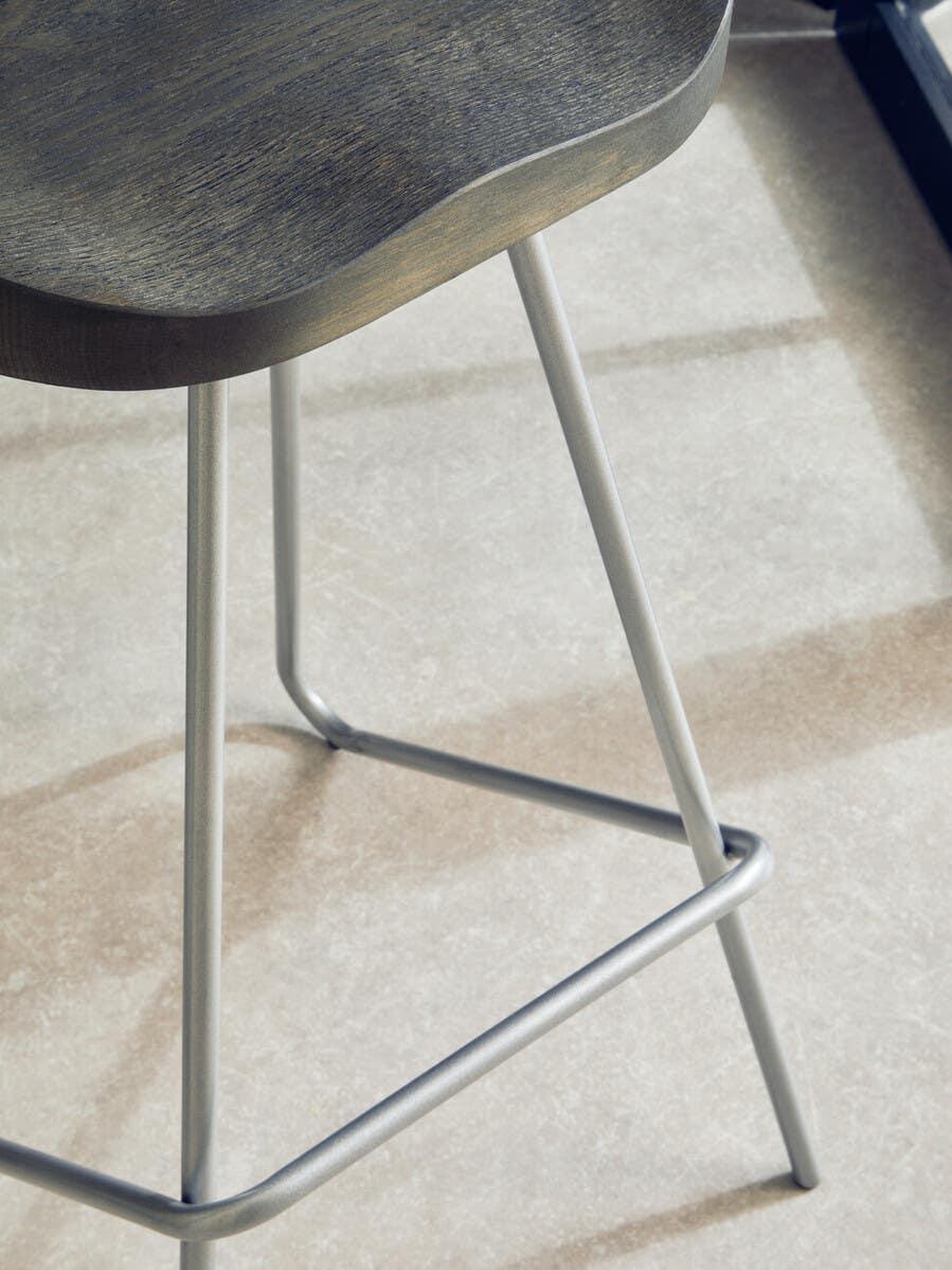 Dark wooden bar stool seat with curved edge and silver metal legs on tiled floor