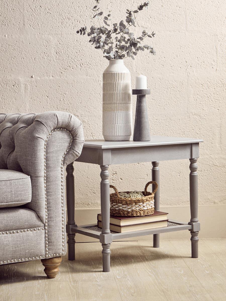 Grey wooden side table with lower shelf, books, woven basket, vase and candle display