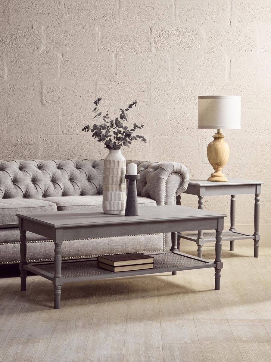 Grey wooden coffee table with vases and books in front of a tufted sofa