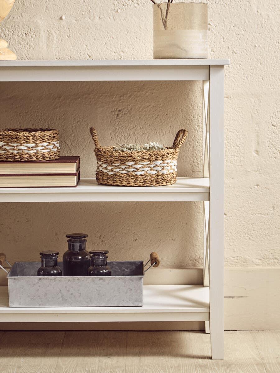 White wooden console table with wicker baskets and vases, styled against a textured wall