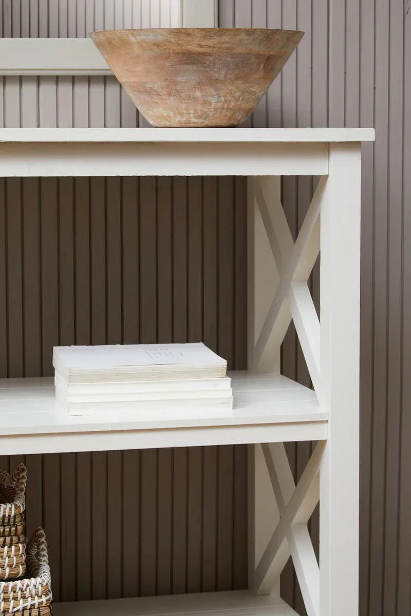 White wooden shelving unit with cross side detail, wooden bowl, stacked books, wicker baskets