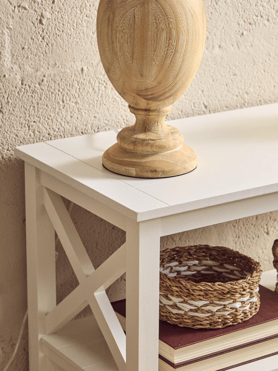 White wooden console table with X side detail, wicker basket, books, and wood lamp base