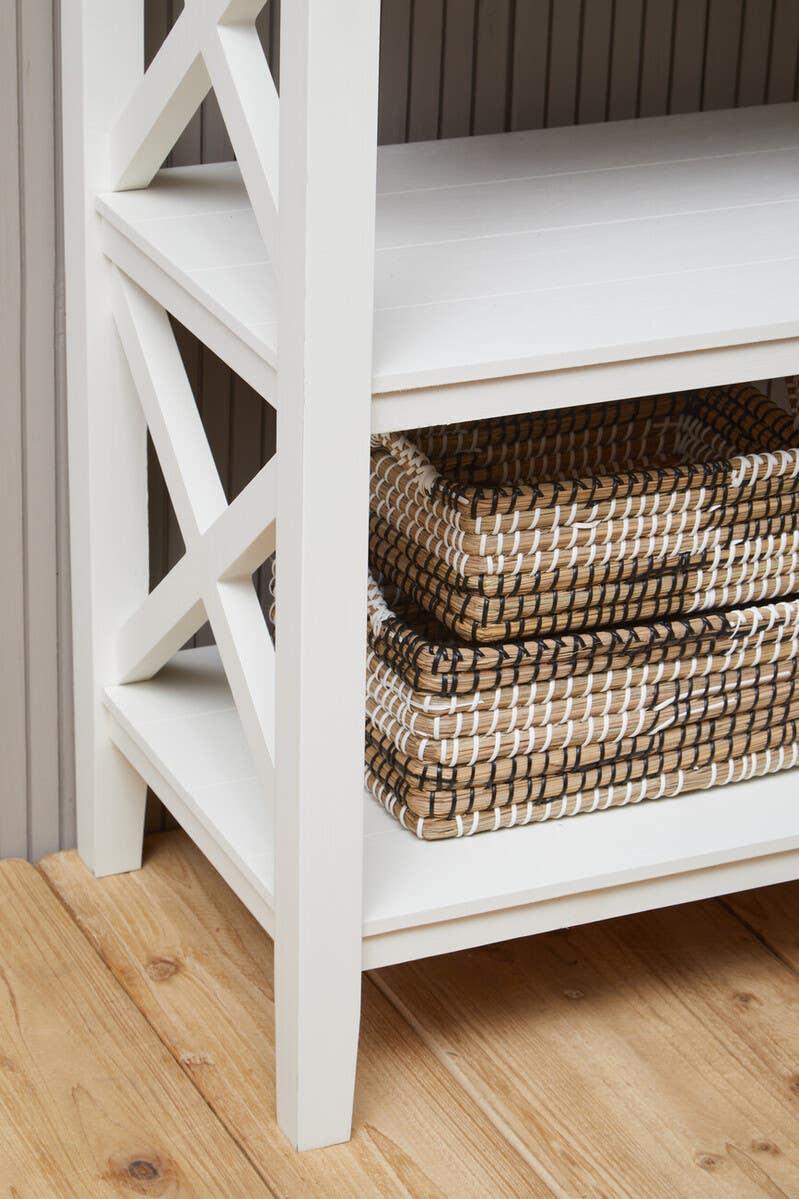 White wooden shelving unit with lower shelf holding stacked woven storage baskets