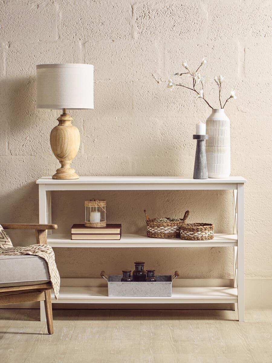 White console table with shelves, styled with lamp, vases, books and woven baskets