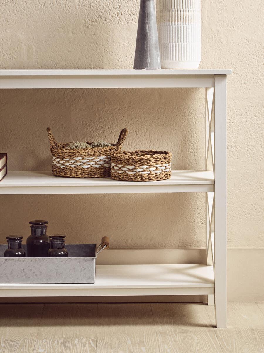 White console table with decorative baskets and metal tray on wooden floor