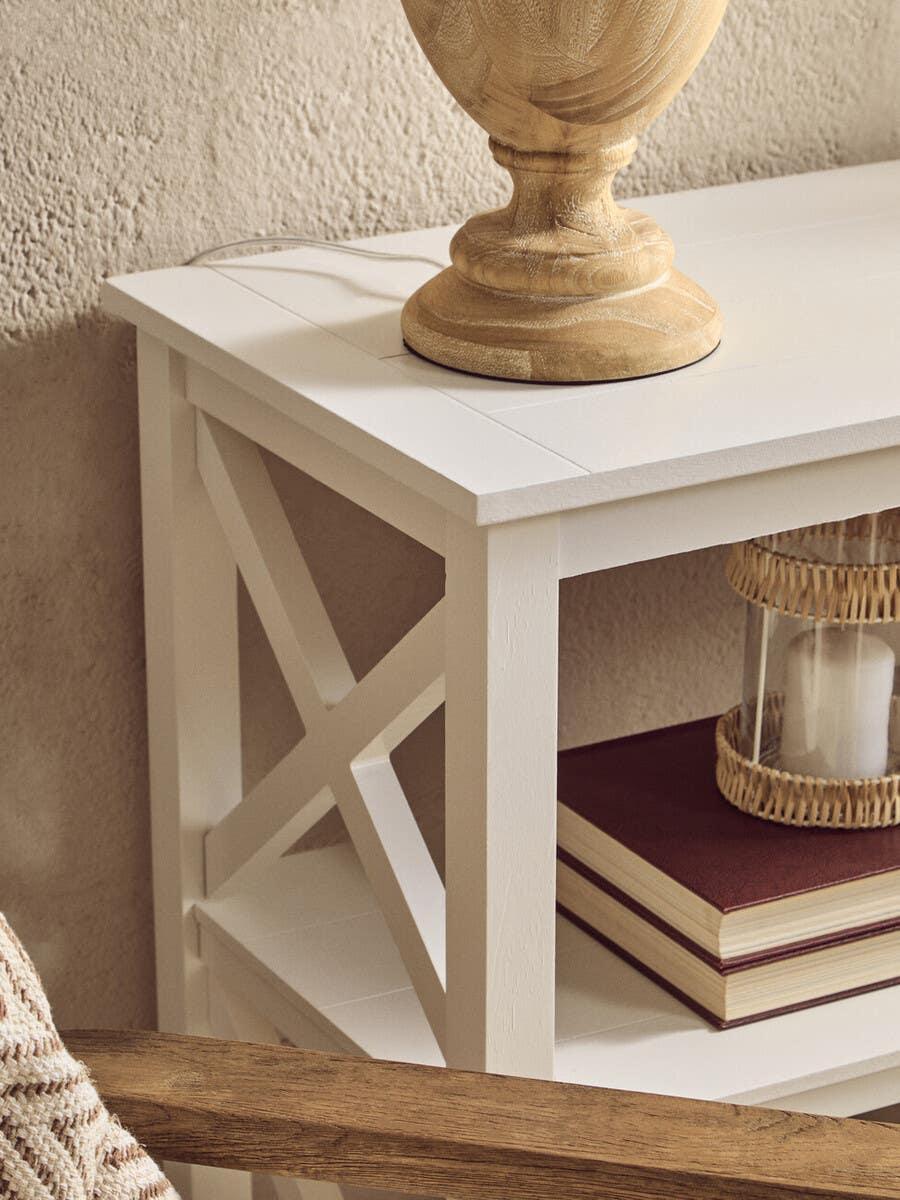 White wooden console table with cross detail, stacked books and decorative lamp