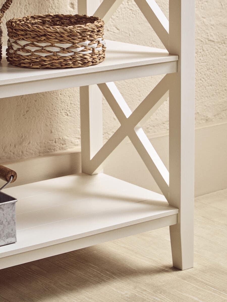 White wooden shelving unit with X-frame detail and woven storage basket on shelf
