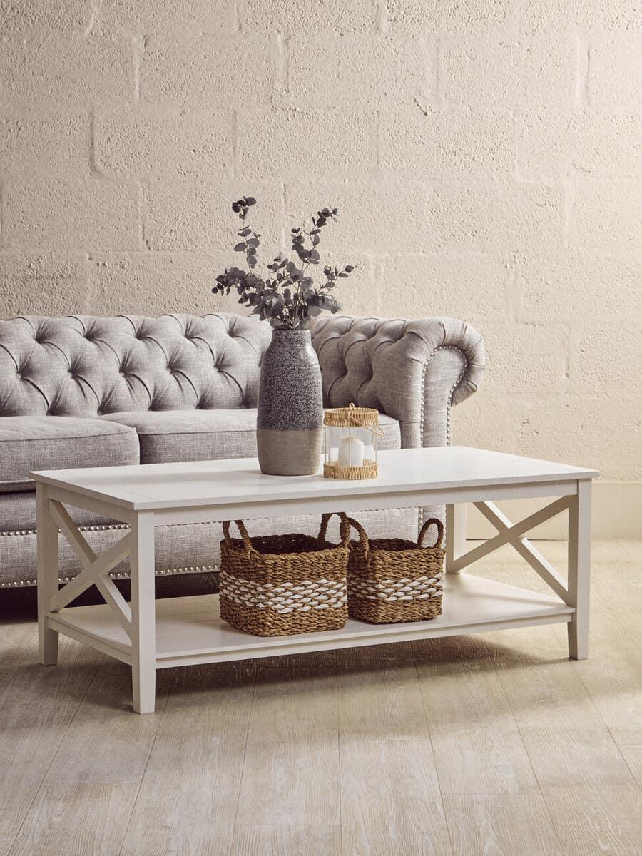 White wooden coffee table with storage shelf, wicker baskets, and vase, in front of grey sofa