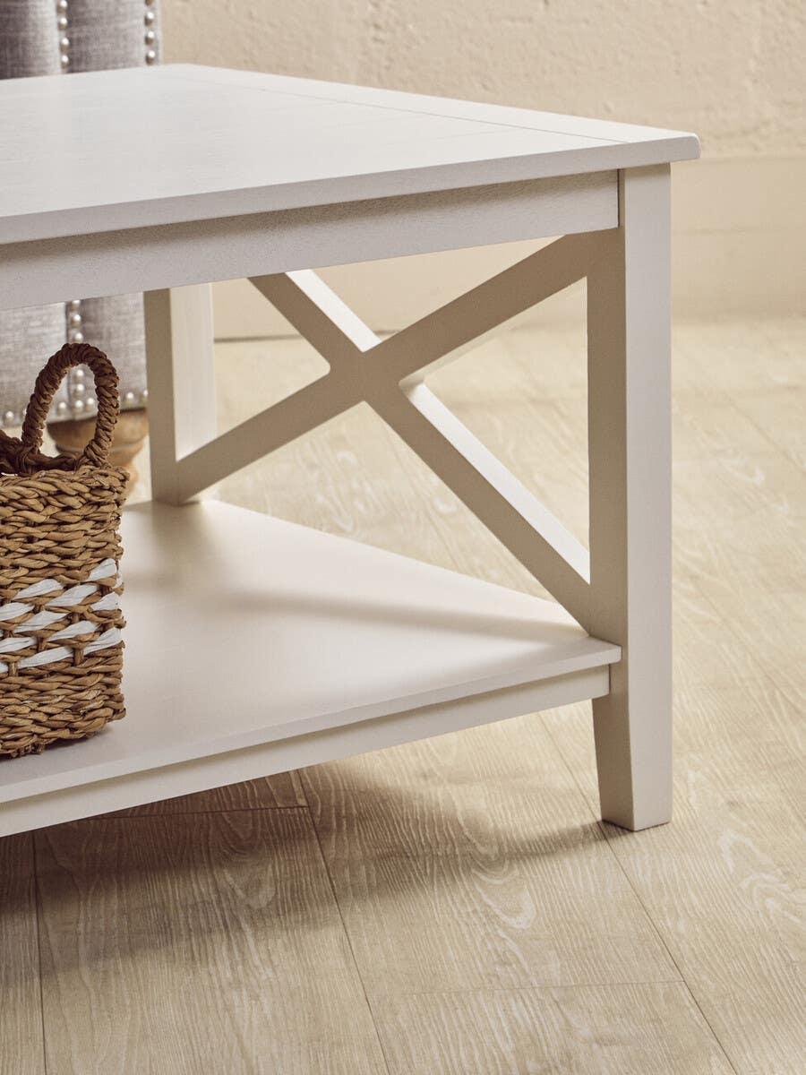 White wooden coffee table with lower shelf and cross-brace detail, basket placed underneath