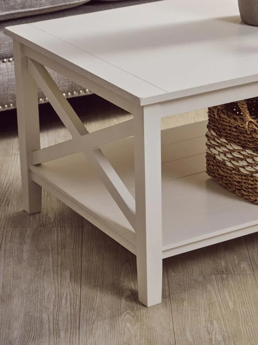 White wooden coffee table with lower shelf and cross side detail on wood floor