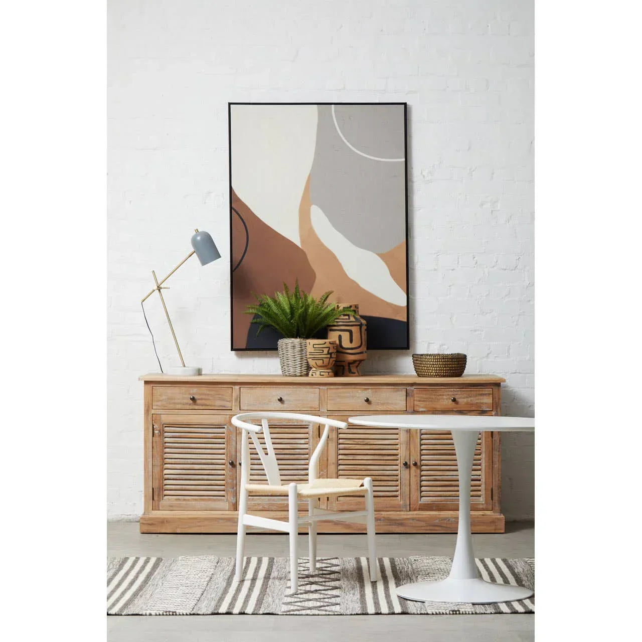 Wooden sideboard with drawers, white dining table, chair, abstract art, and decor pieces