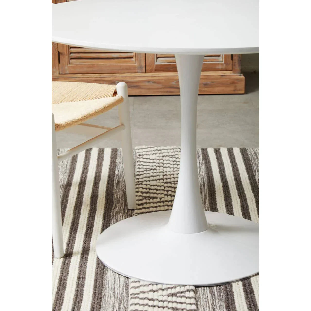 White round dining table with pedestal base and woven chair on striped rug