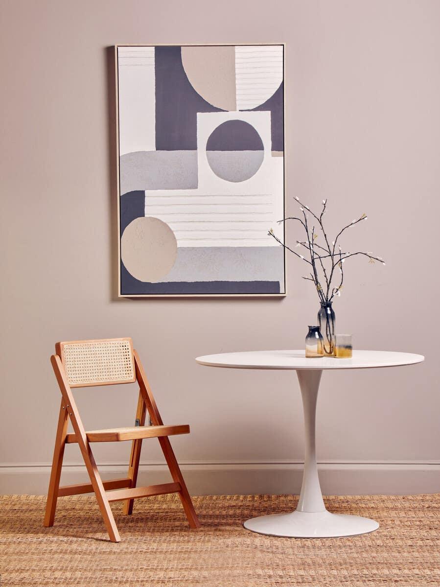 Wood folding dining chair beside round white table on woven rug with modern wall art