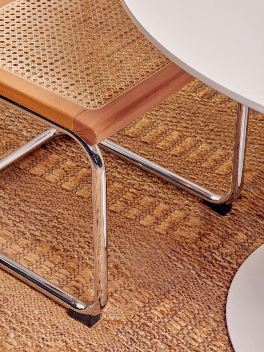 Cane seat dining chair with chrome legs beside white round table on woven rug