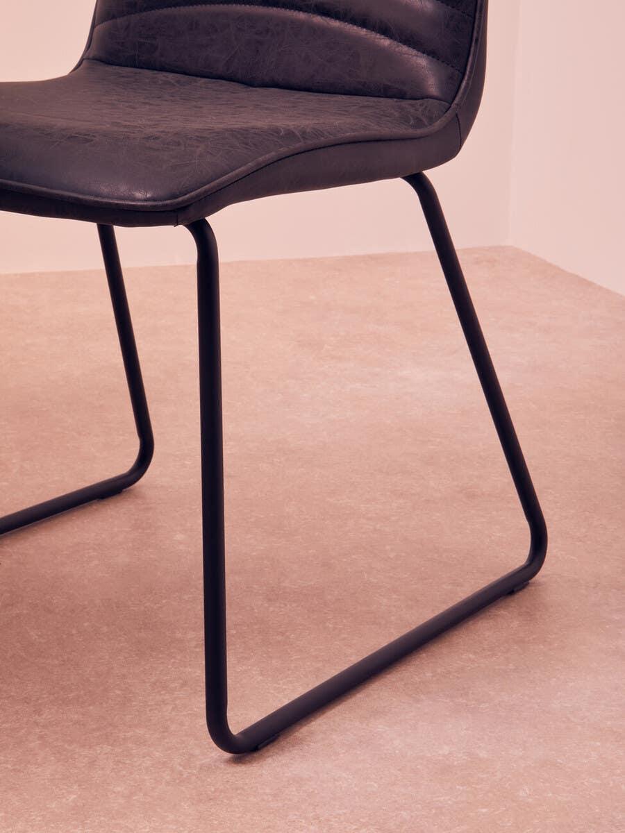 Modern dining chair with black metal legs and padded faux leather seat, side angle view