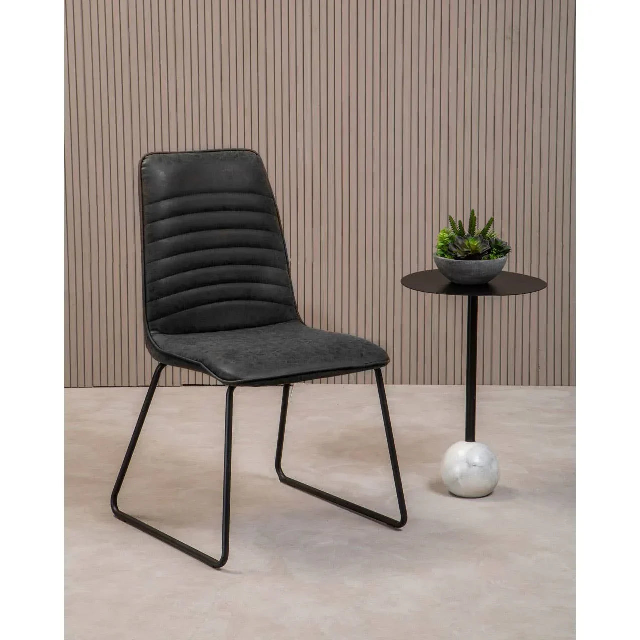 black dining chair with metal legs beside small round table with potted plant