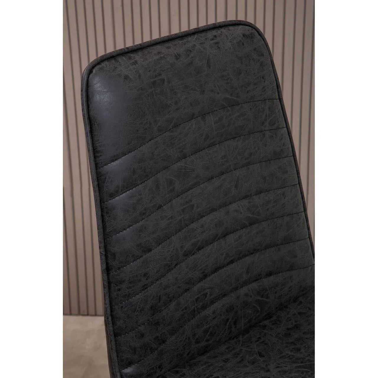 Black faux leather dining chair with stitched detail and curved backrest close-up