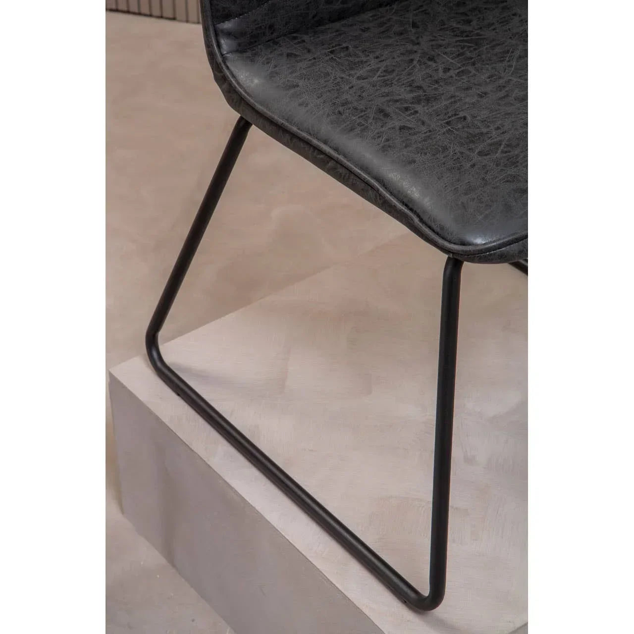 Closeup of black faux leather dining chair seat with metal sled base on light flooring