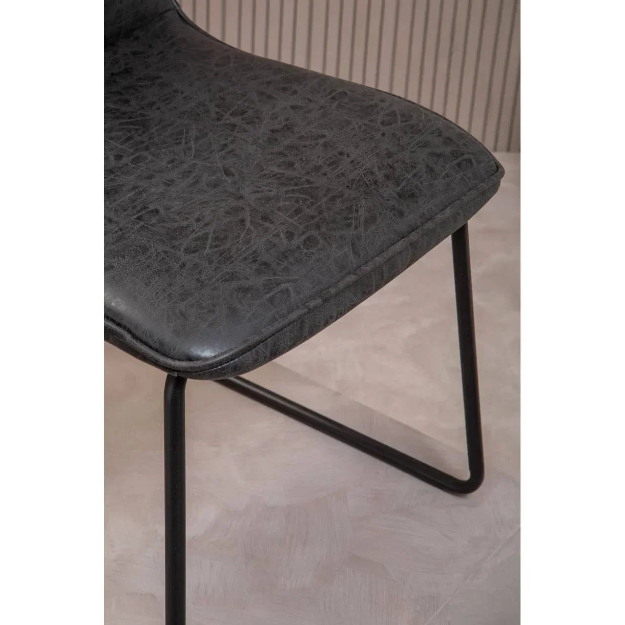 Black faux leather dining chair seat with metal legs on light flooring