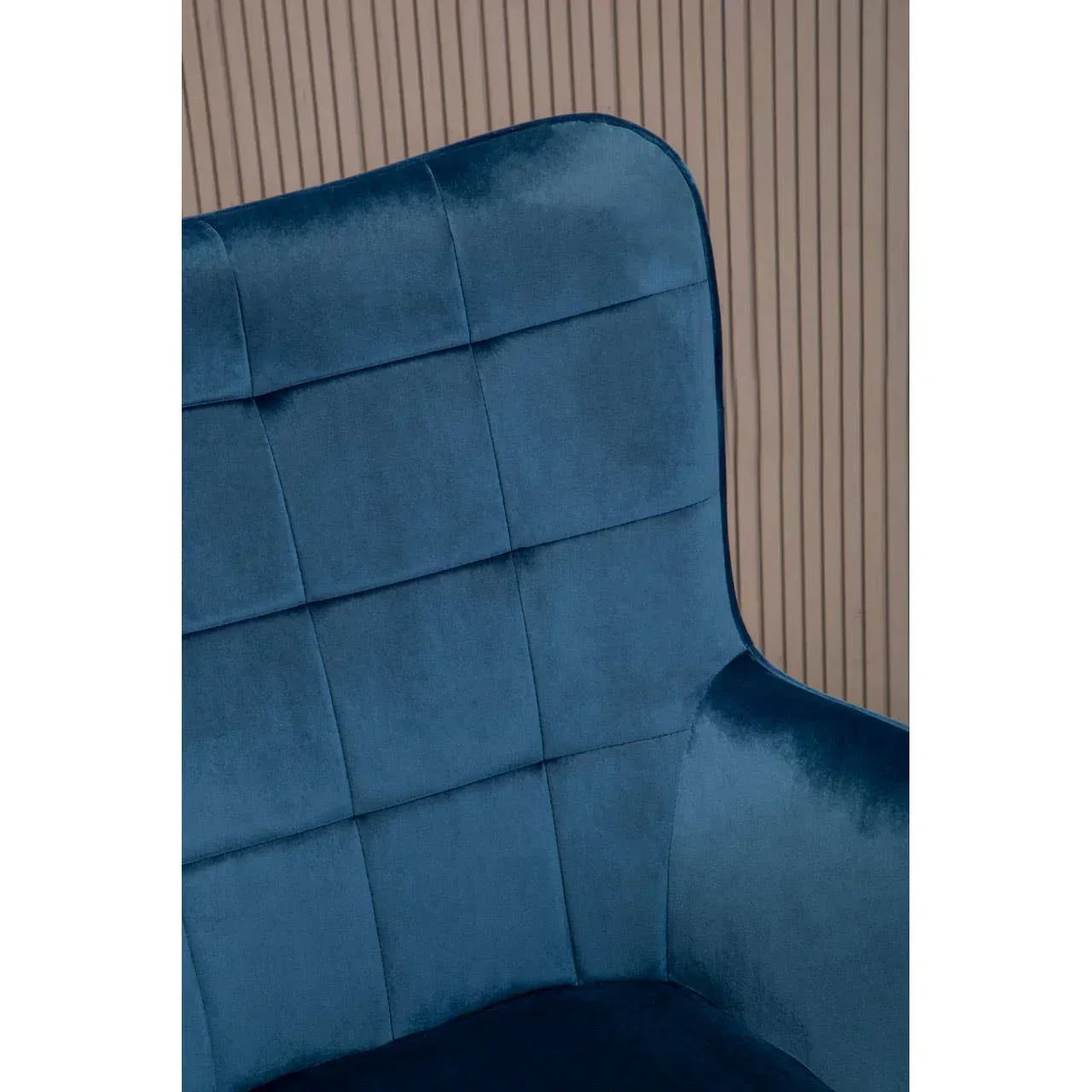 Close-up of blue velvet armchair with grid stitched backrest against beige panelled wall