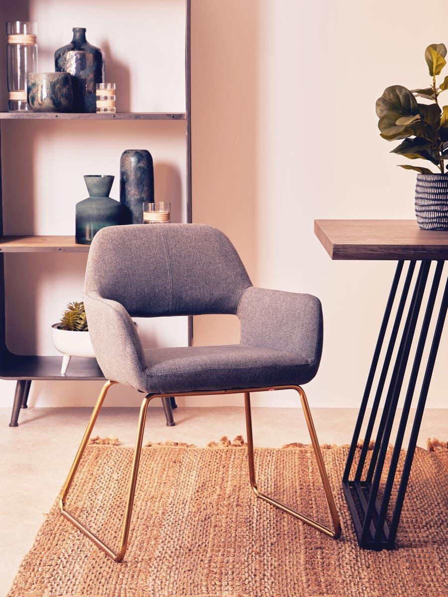 Grey upholstered dining chair with gold metal legs beside wooden table on jute rug