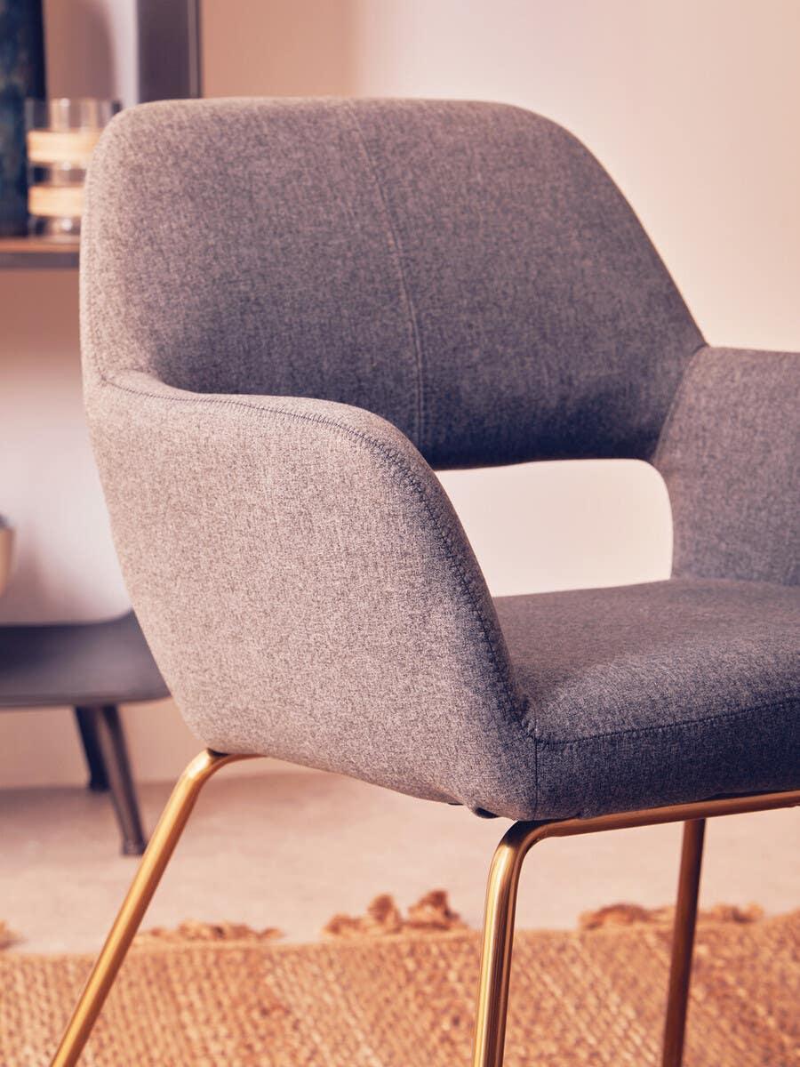 Grey fabric dining chair with gold metal legs on woven rug