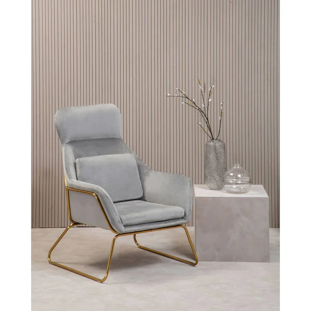 Grey velvet accent chair with gold frame beside a modern side table and decorative vases