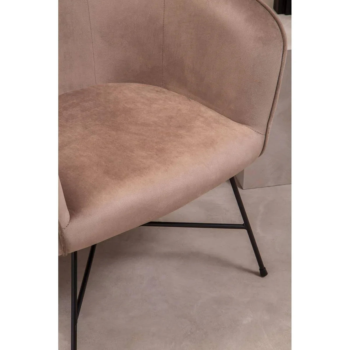 Closeup of beige upholstered chair seat with curved backrest and black metal legs on stone floor