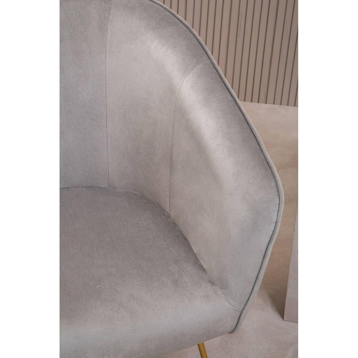 Close-up of grey velvet accent chair with curved backrest and gold metal leg