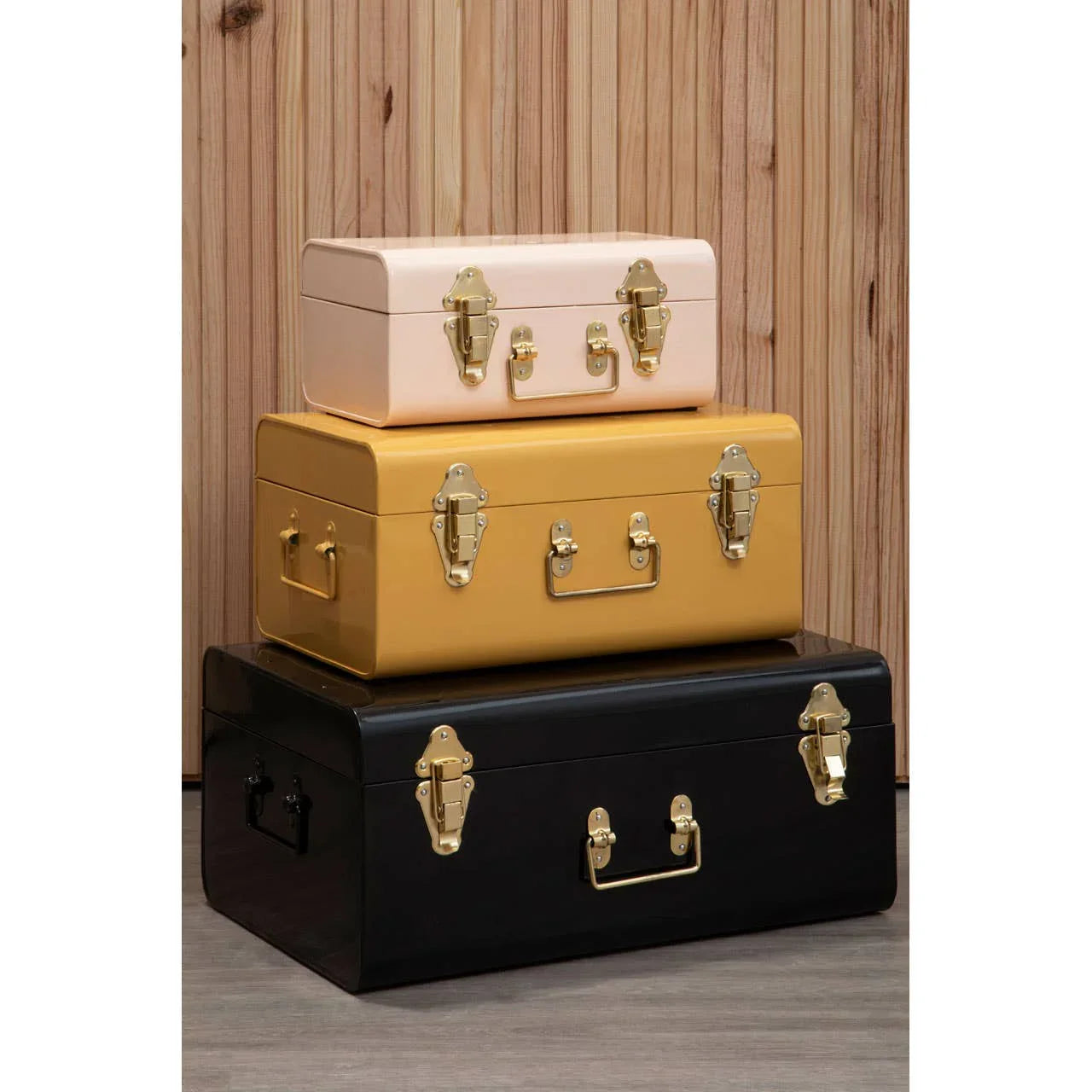Stacked storage trunks in pink, yellow and black with gold clasps against wood panel wall