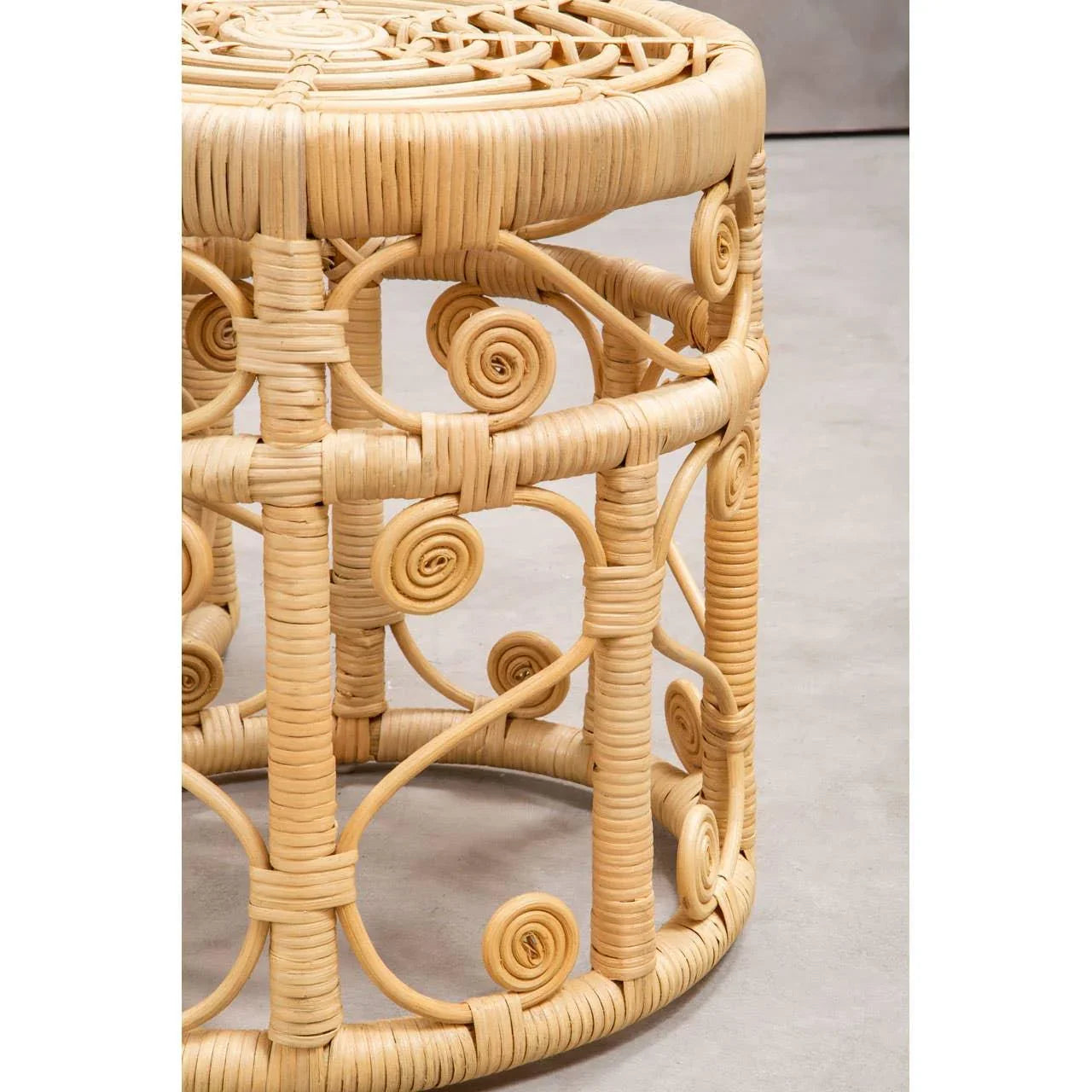Natural rattan side table with round top and spiral woven pattern on grey floor